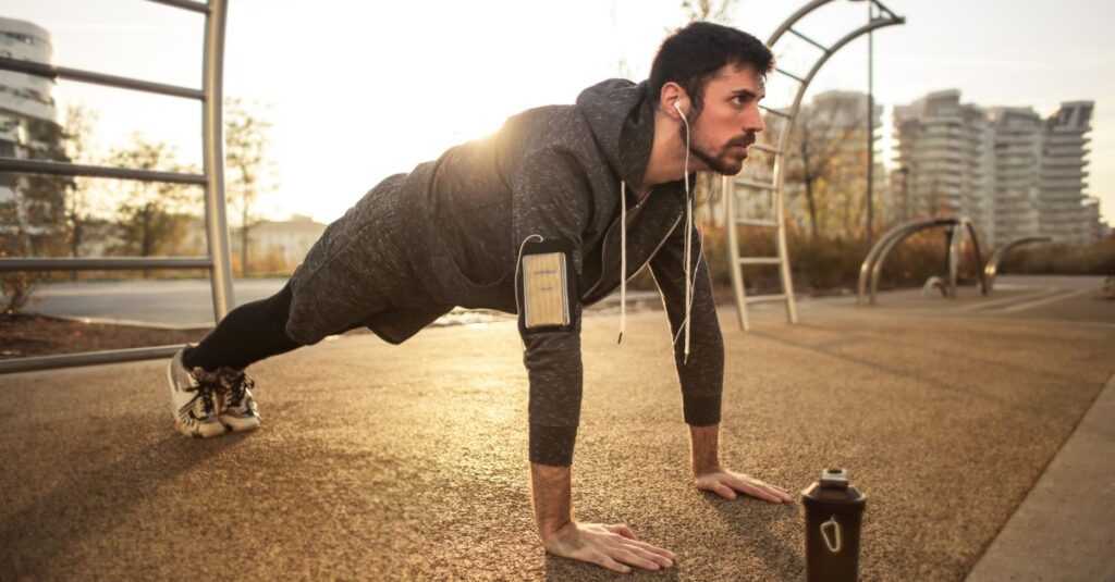 Adult man doing push-ups outdoors with earphones during sunrise, showcasing fitness and healthy lifestyle. — how to increase