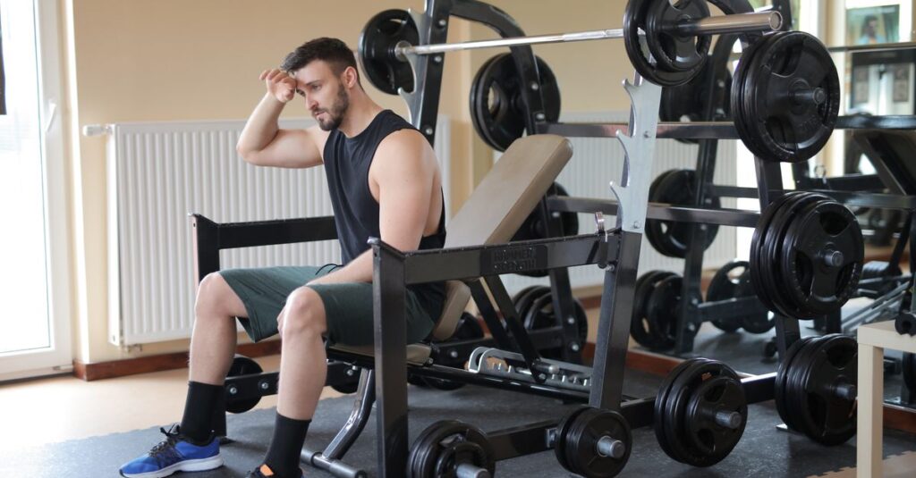 Man taking a break in a gym setting, sitting beside loaded weight bench, looking thoughtful. — symptoms for low testosterone
