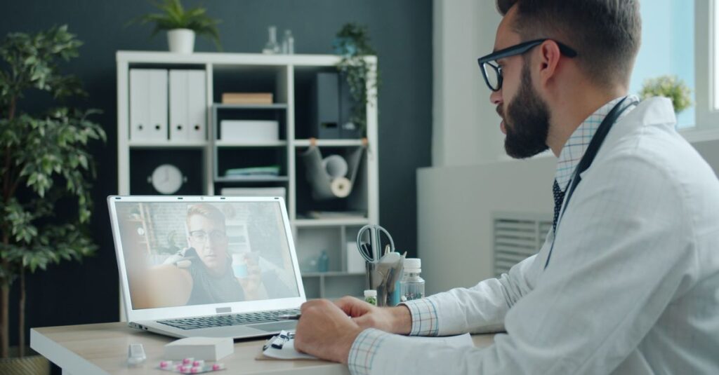 Doctor in white coat video calling a patient on a laptop in a modern office setting. — How to Choose a Legit Telehealth Longe