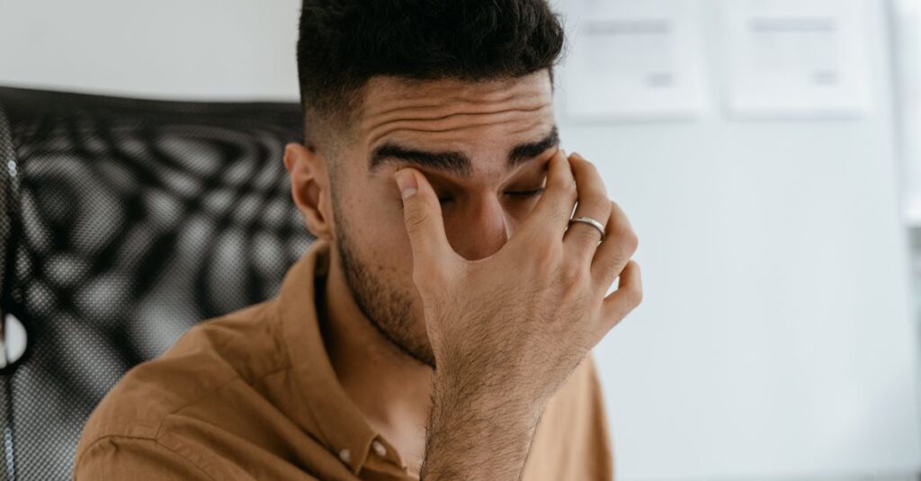 Close-up of a man rubbing his eyes, capturing stress or fatigue in an office environment. — low cortisol