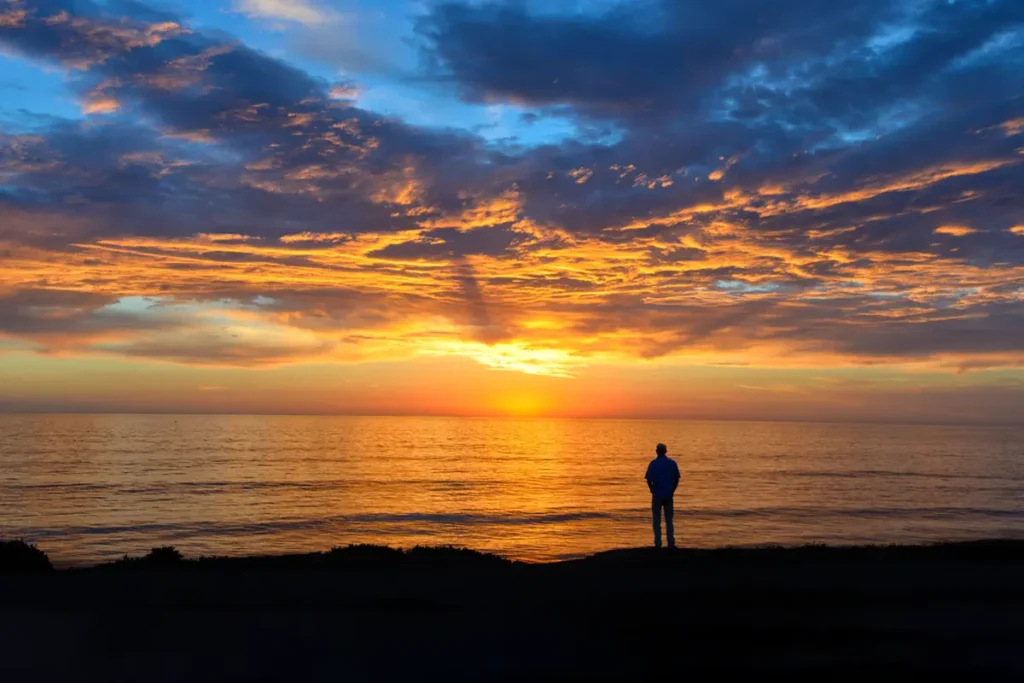 Silhouette of a person standing on a beach under a cloudy sky during a breathtaking sunset