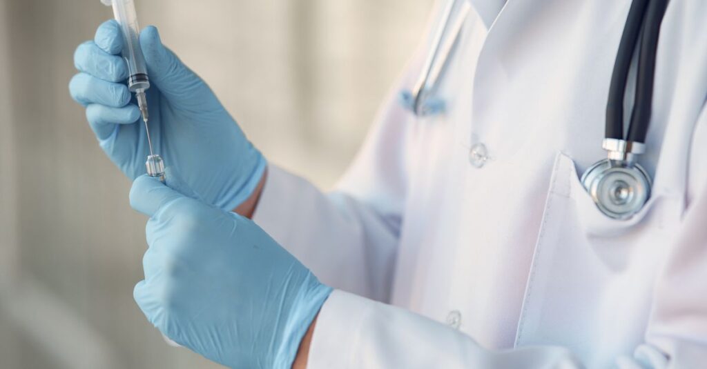 Healthcare professional wearing gloves and holding a syringe in a clinical setting. — peptide injections